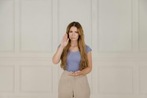 A woman in a blue t-shirt using sign language. Neutral background enhances focus on communication.