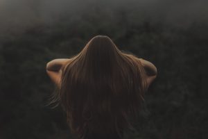 Back view of a woman with long hair, standing in a misty forest.