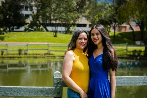 A joyful mother and daughter pose by a pond in a sunny park, exuding happiness.