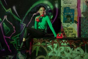 Young woman in vibrant setting surrounded by urban graffiti, holding a red retro phone, exuding a punk vibe.