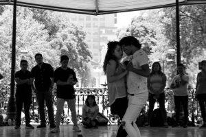 A couple dances passionately in a park pavilion surrounded by an intrigued crowd.