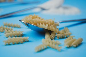 Close-up view of uncooked fusilli pasta spirals on a spoon with a blue background.
