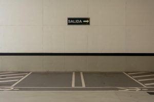 Minimalist urban parking area with a 'SALIDA' exit sign pointing right on the wall.
