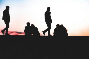 A group of silhouettes walk and sit against a vibrant sunset sky.
