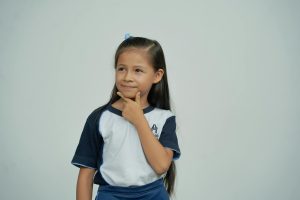 A young schoolgirl in uniform stands thoughtfully against a white background.