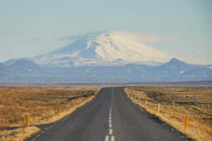 Empty road leading to a snow-covered mountain in Iceland under a clear blue sky.