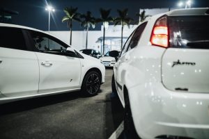 White cars gathered at a nighttime car meet in an illuminated parking lot.