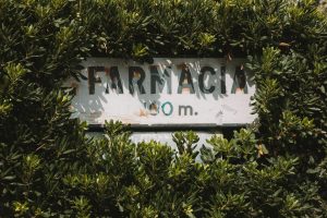 A vintage "Farmacia" sign surrounded by lush green leaves in Benidorm, Spain.
