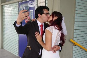 Bride and groom kiss while capturing a selfie, celebrating their wedding day.