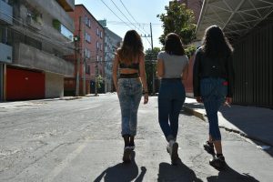 Three women walking down a city street, captured from behind, showcasing urban fashion style.