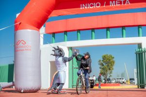 A cyclist receives a high-five from a mascot at the finish line of a cycling event under a clear blue sky.
