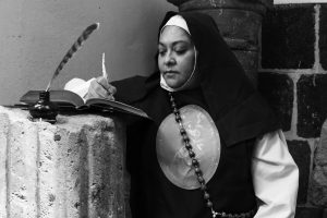 A contemplative nun writes with a quill in a serene religious setting in Mexico City.