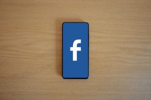 Smartphone with Facebook logo on screen, placed on a wooden background. Top view.