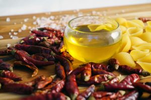 Chili peppers, pasta, and olive oil on a wooden board create a vibrant Italian food composition.