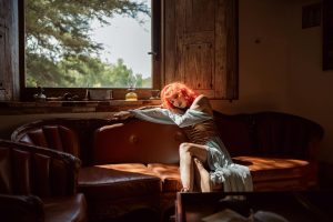 A woman with red hair sitting on a classic sofa in a rustic room lit by natural light.
