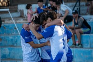 A group of young soccer players share an emotional hug on the field during an outdoor game.