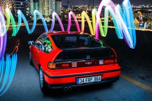 Red Honda CRX parked at night with colorful light trails in Ankara's cityscape.