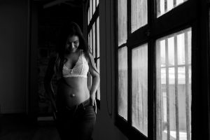 Artistic black and white portrait of a woman in a lace top near a window.