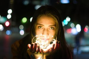 A young woman holding string lights at night, creating a magical and mysterious ambiance.