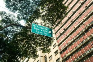 Street sign pointing to R. Augusta, Bela Vista, Zona Sul in São Paulo with urban backdrop.