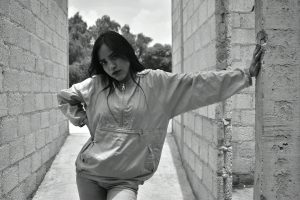 Black and white photo of a young woman posing confidently between brick walls in an urban setting.