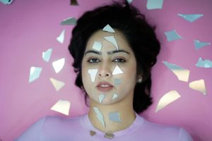Artistic portrait of a woman surrounded by mirror shards on a pink background, creating a surreal effect.