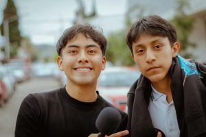 Portrait of two young men posing and smiling with a microphone outdoors on a street.