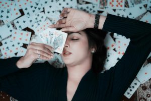 Woman lying on playing cards, holding three face cards, creating a creative and stylish scene.