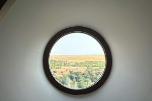 A scenic view of Segovia's landscape through a circular window, showcasing lush greenery and fields.