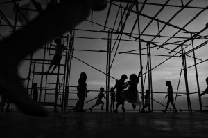 Black and white image of children silhouetted against the sky, playing on scaffolding.