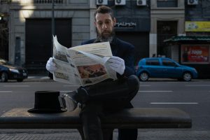 A stylish man in formal attire reads a newspaper on a bench in Buenos Aires.