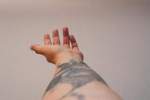 A close-up of a tattooed arm reaching out against a neutral beige background, showcasing body art.