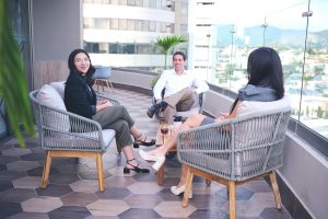 Three adults enjoying drinks on a rooftop terrace with urban views. Casual business setting.