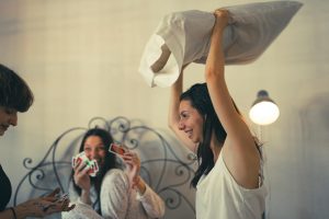 Three women enjoying a playful game night and pillow fight indoors.