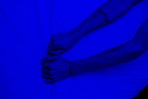 Close-up of tattooed arms pulling fabric under intense blue lighting, symbolizing stress or frustration.