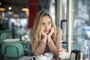 A thoughtful woman with blond hair sitting in a cozy café, enjoying a hot drink.