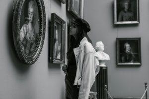 Black and white photo of a woman admiring paintings in a museum gallery.