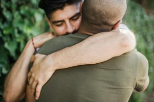 Intimate moment between two men sharing a warm hug outdoors, captured in natural light.
