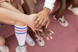 From above of crop unrecognizable diverse friends stacking hands before competition on sports ground on sunny day