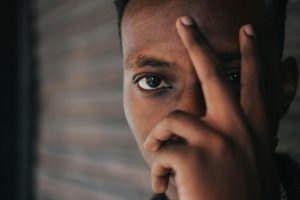 Crop anonymous young African American male covering eye with hand and looking at camera while standing on street