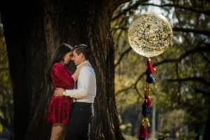 A loving couple embraces under a large tree with a balloon reading 'Aquí empieza nuestra historia'.