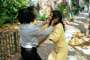 Anonymous black child touching face of cheerful ethnic girlfriend while playing on pavement and looking at each other in autumn