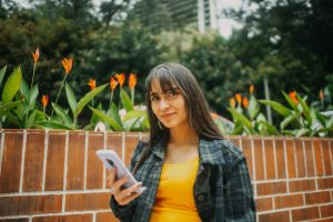 Woman in yellow top using smartphone, surrounded by vibrant flowers in Guatemala.