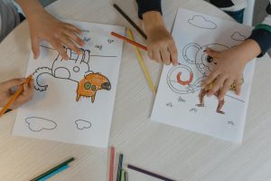 Children using colored pencils to bring animal drawings to life on a wooden table.
