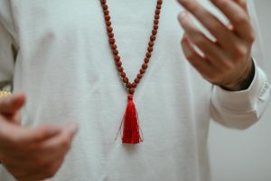 A detailed focus on hands showcasing a rudraksha mala necklace with red tassel.