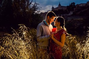 A couple shares a tender moment in the sunset glow with Toledo's historic skyline in the background.