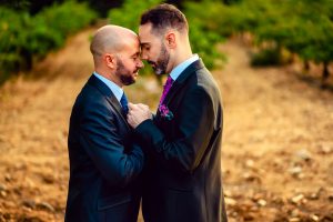 Two men in suits embrace tenderly in an outdoor setting, symbolizing love and unity.