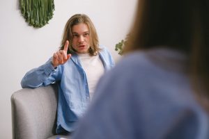 A therapist gestures while talking to a patient in a relaxed indoor environment.