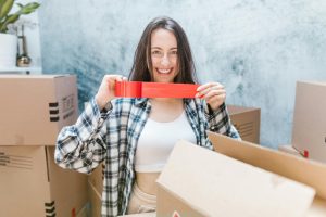 Caucasian woman packing boxes with red tape, smiling in an indoor setting. Perfect for moving and relocation themes.