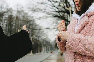 Crop unrecognizable female in warm coat using sign language standing on blurred street and communicating with faceless friend